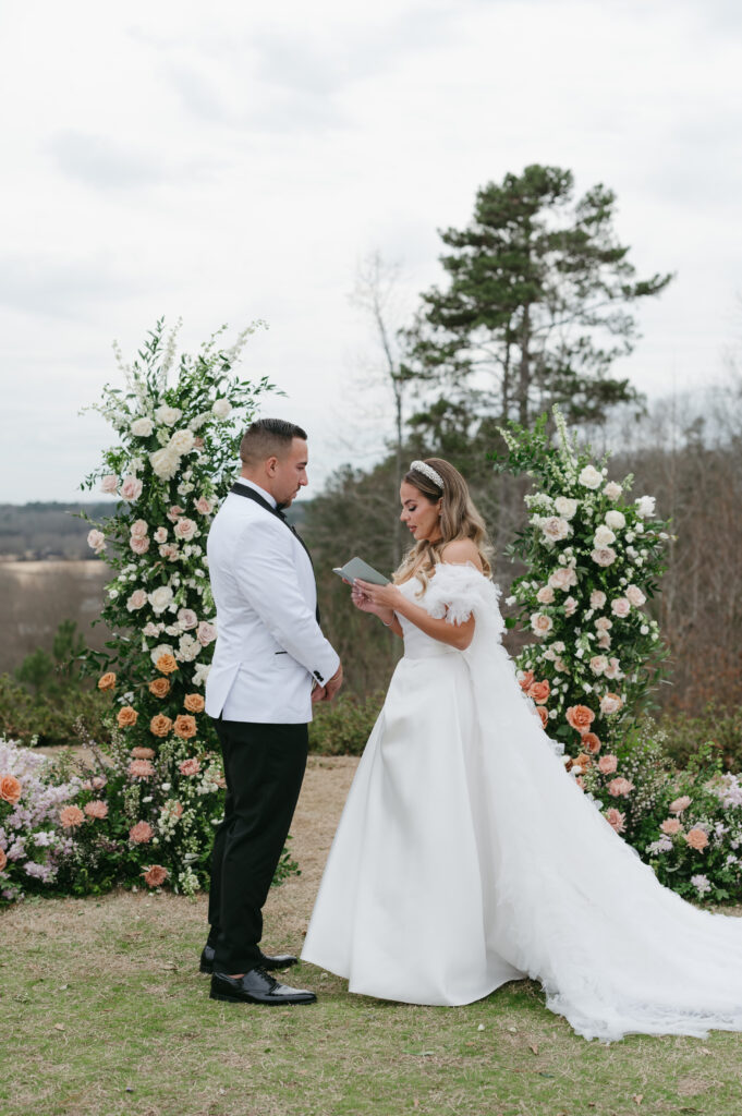 The couple exchanges vows at their colorful luxury wedding at Foxhall Resort in front of a broken floral arch and an aisle full of flowers. | Megan Kuhn Photography