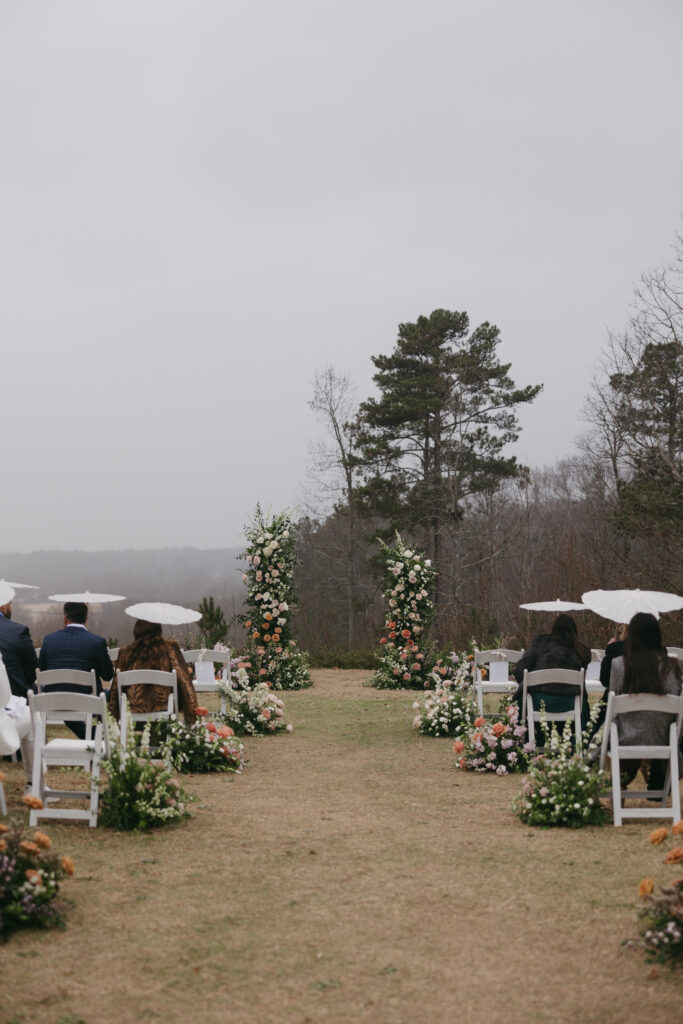 This colorful outdoor wedding at Foxhall Resort had a broken floral arch and an aisle full of flowers. Guests held parasols. | Megan Kuhn Photography