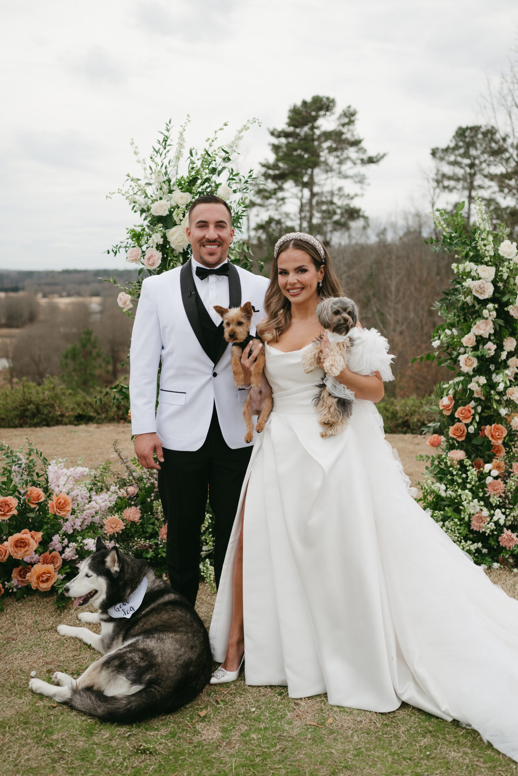 Modern wedding portraits with a bride with a bridal headband and groom with a white suit and their dogs in front of their colorful floral arch. | Megan Kuhn Photography